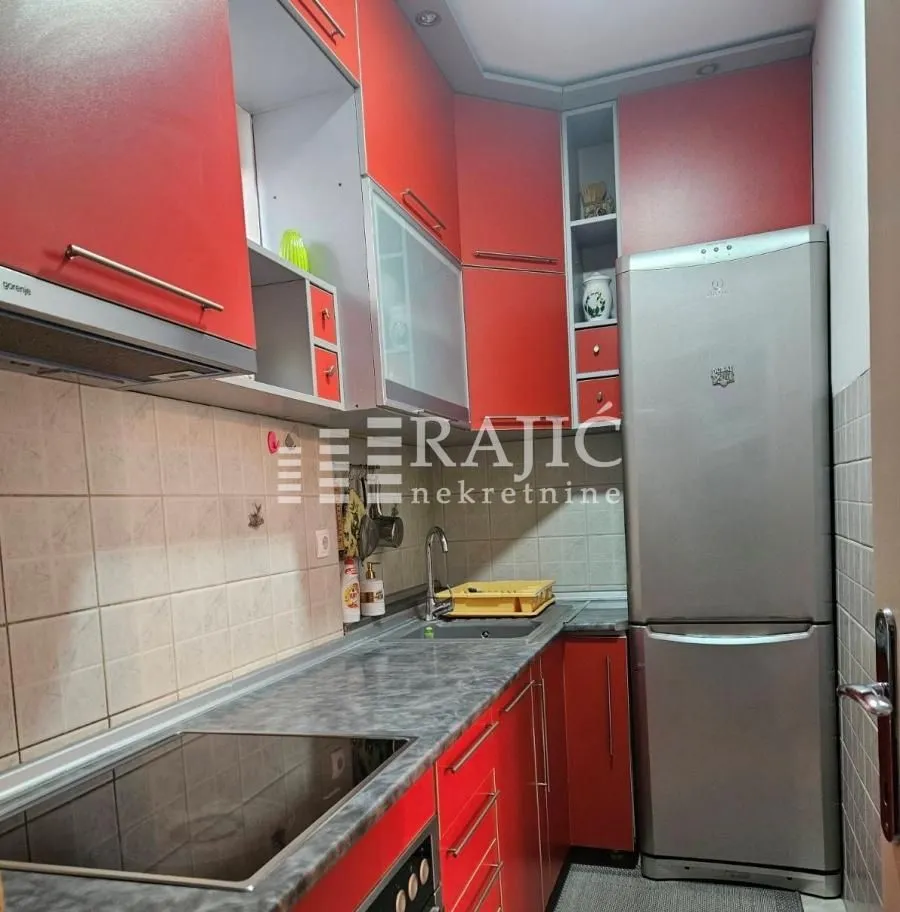 View of a small kitchen with red cabinets and a refrigerator.