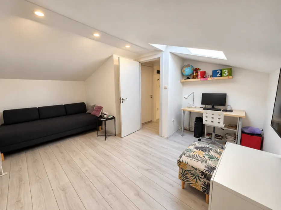 Attic living room with a sofa, desk, and skylight.