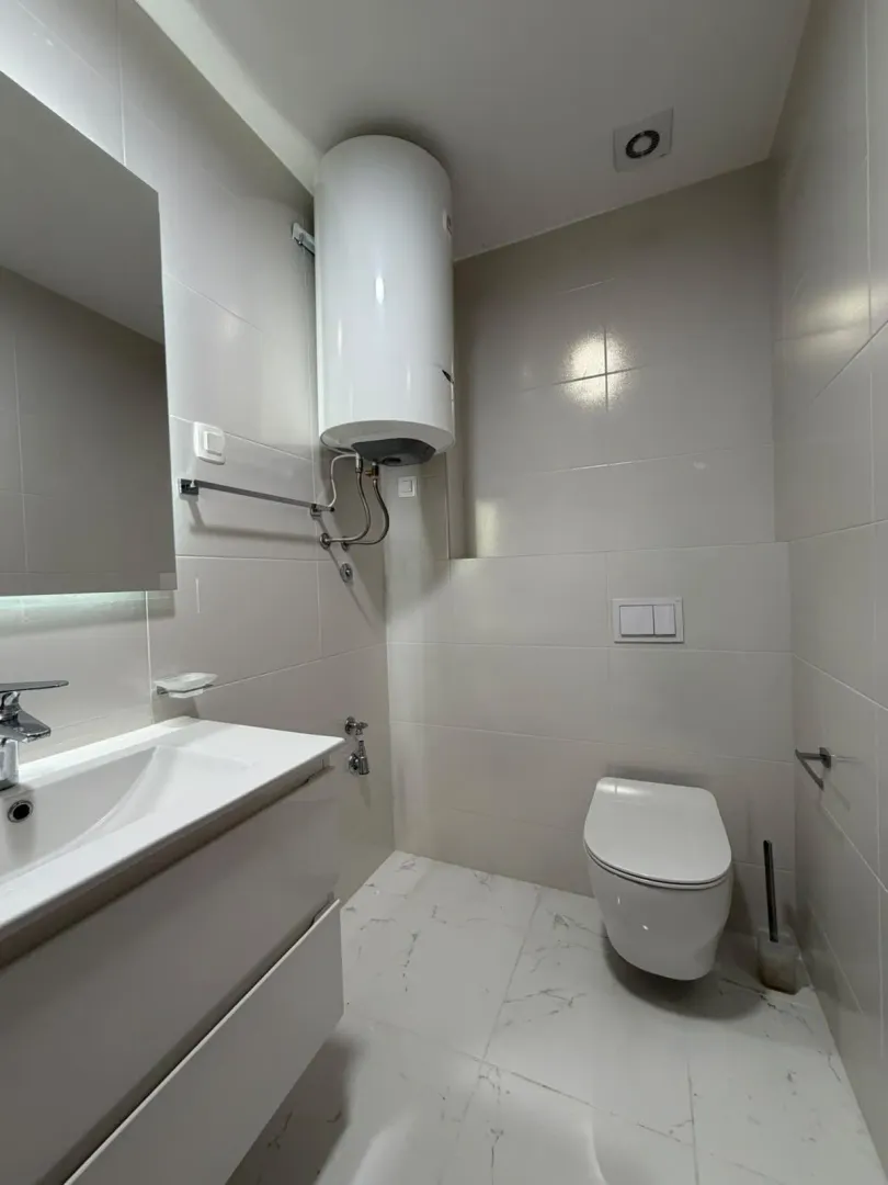 Modernly equipped bathroom with white tiles, washbasin and toilet.