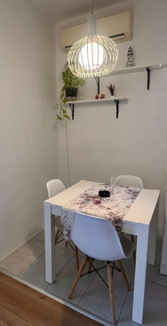 Manji trpezarijski sto sa bijelim stolicama i ukrasnom rasvjetom.