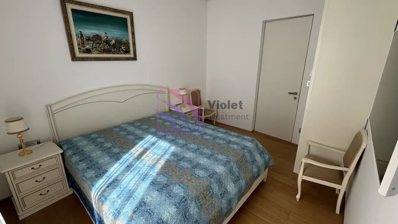 Namještena spavaća soba sa bračnim krevetom, noćnim stočićima i stolicom.