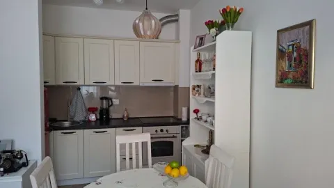 Manja kuhinja u svijetlim tonovima sa trpezarijskim stolom u prvom planu. - image 4