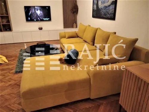 Spacious living room with a large yellow sofa and a wall-mounted TV.