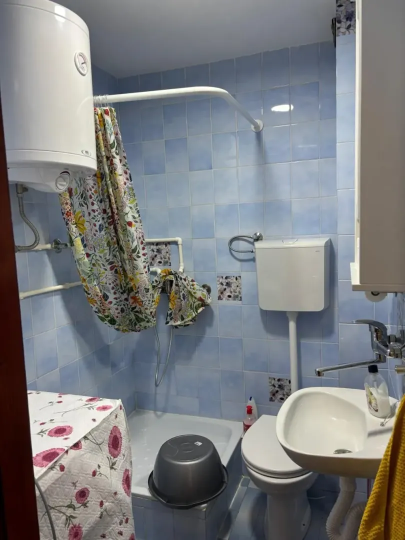 Manje kupatilo sa plavim pločicama, tuš kabinom i bojlerom.
