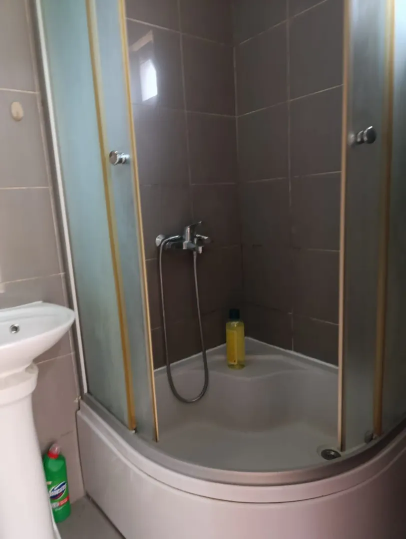 Small bathroom with a shower cabin and a sink in light tiles.