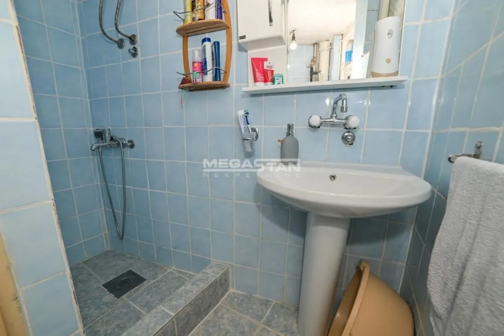 Manje kupatilo obloženo pločicama sa tuš-kabinom i umivaonikom.