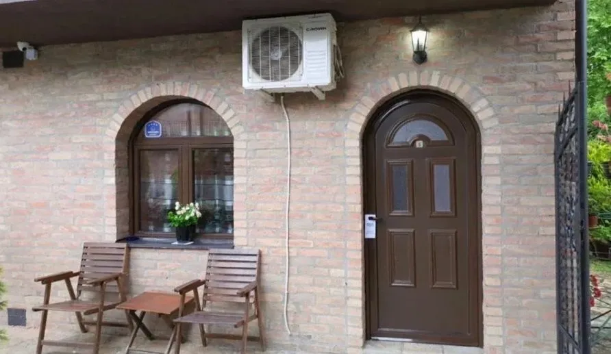Fasada kuće sa ulaznim vratima, prozorom i drvenim stolicama ispred.