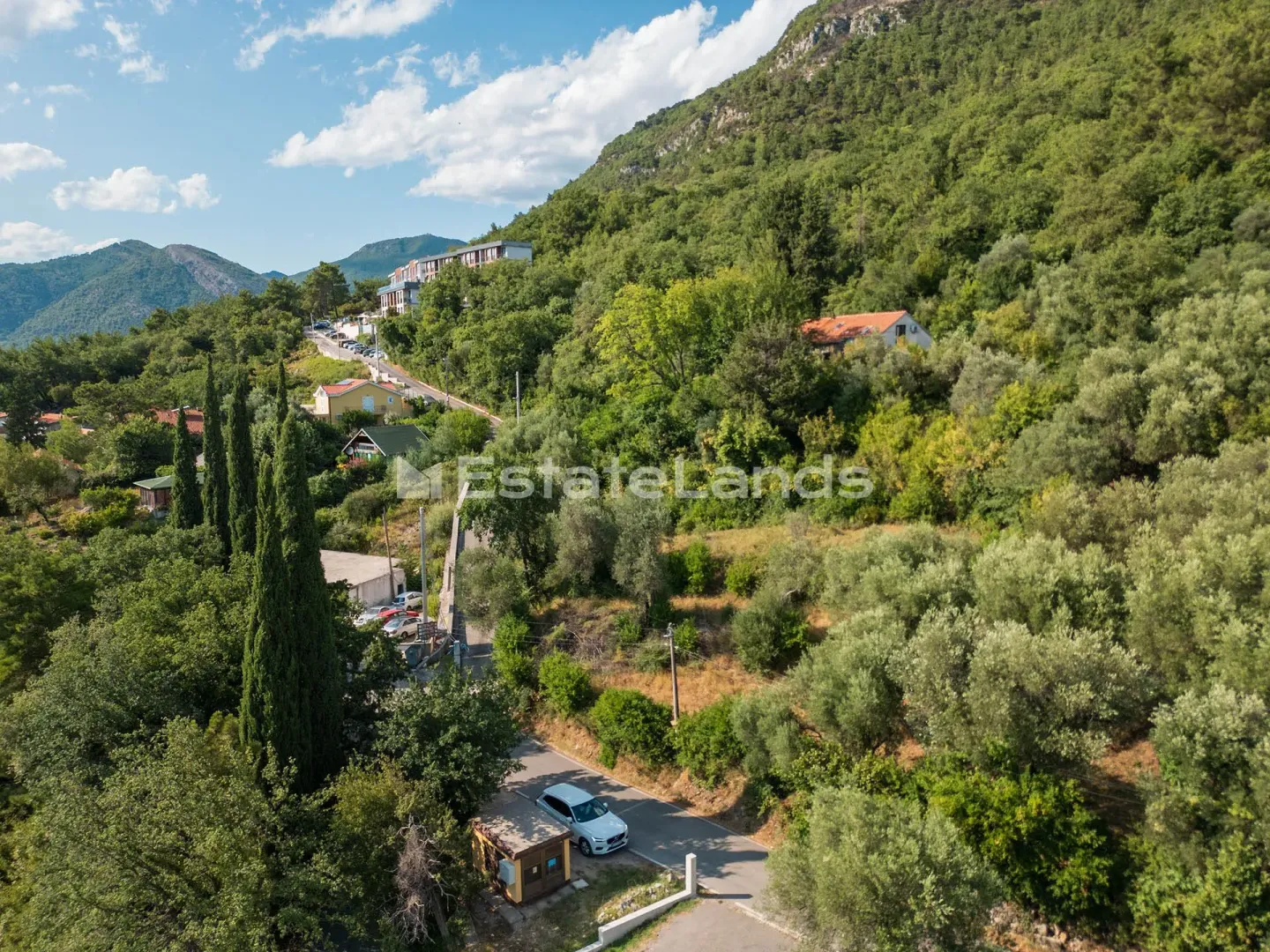 Pogled iz vazduha na prirodu, kuće i zelene površine.