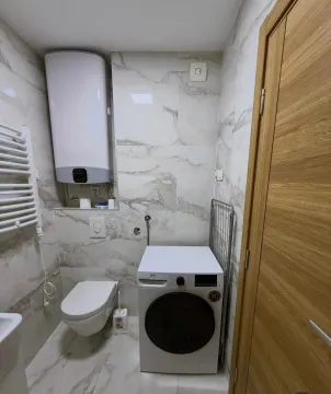Smaller bathroom with tiles, toilet, water heater, and washing machine. - image 9
