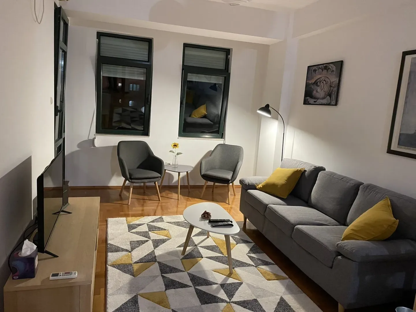 Svijetla dnevna soba sa sivom garniturom, foteljama i modernim tepihom.