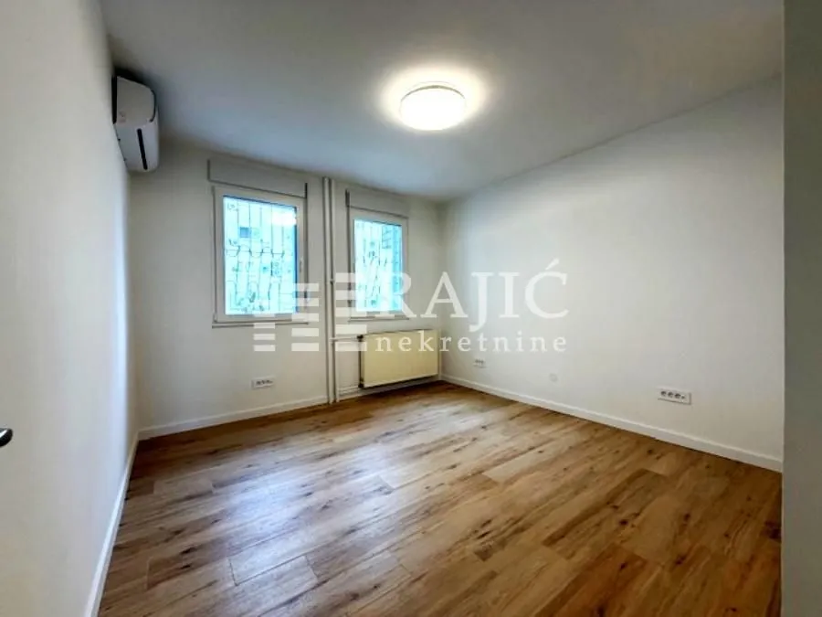 Empty room with wooden flooring and two windows.