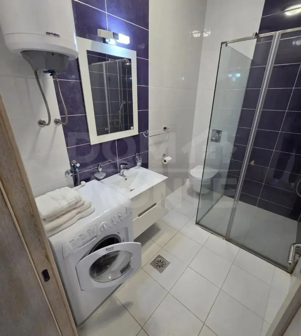 Moderno opremljeno kupatilo sa tuš kabinom i veš mašinom.