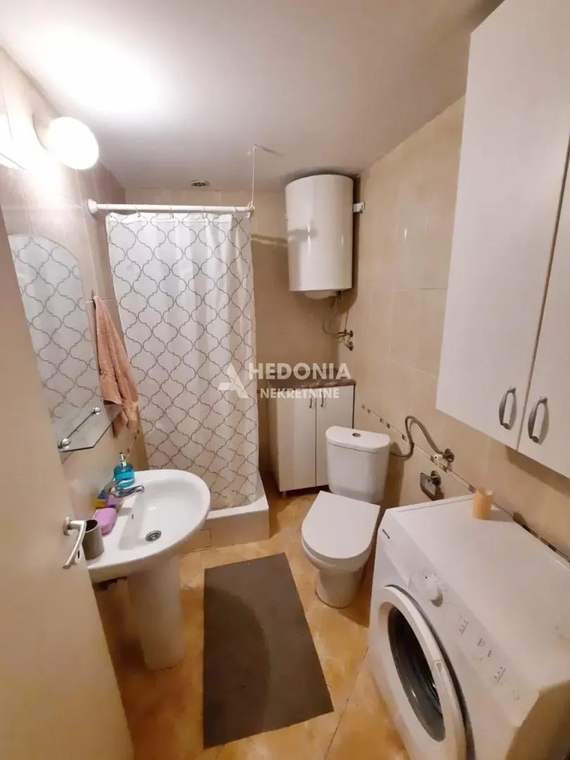 Smaller bathroom with a shower cabin, washbasin, toilet, and washing machine.