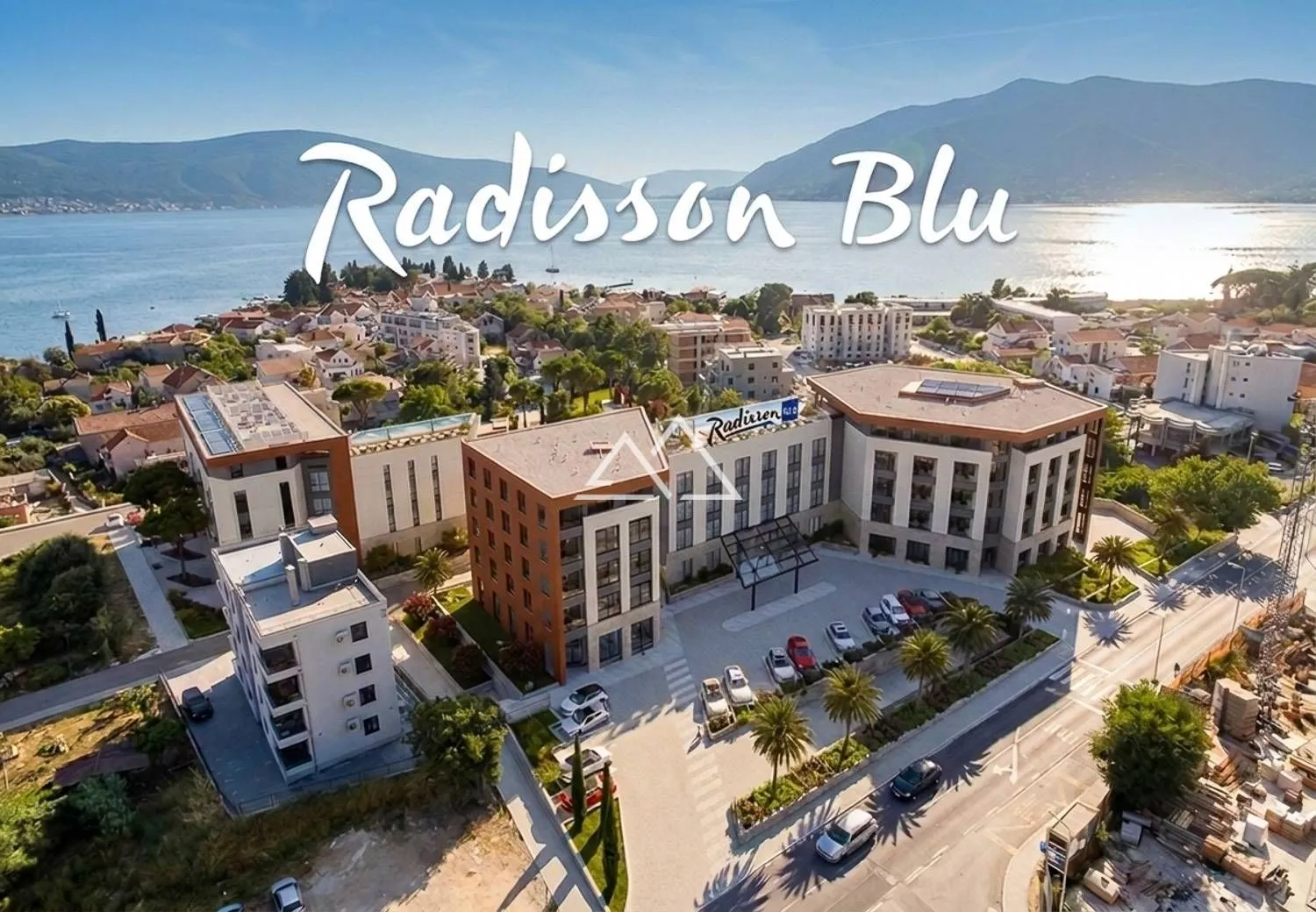 Pogled iz vazduha na hotelski kompleks sa okolnim naseljem i morem u pozadini.