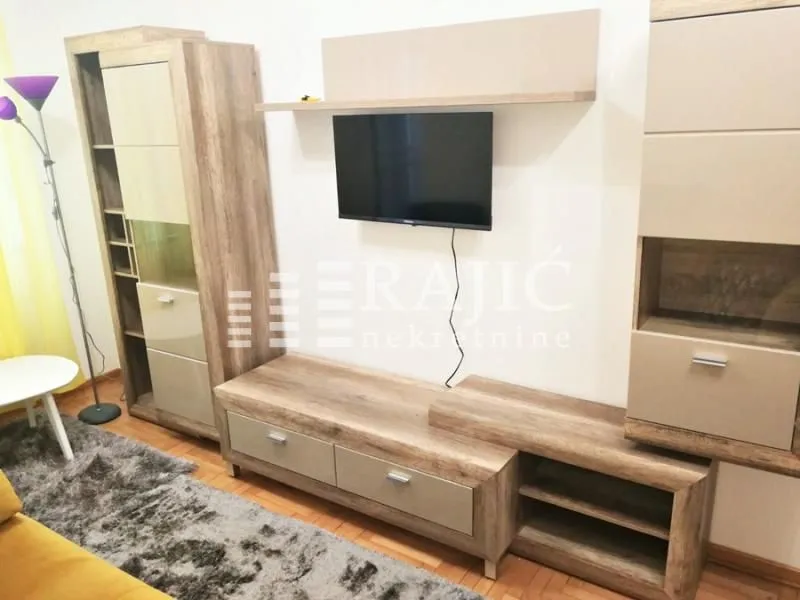 Living room furnished with wood-toned furniture and a wall-mounted TV.