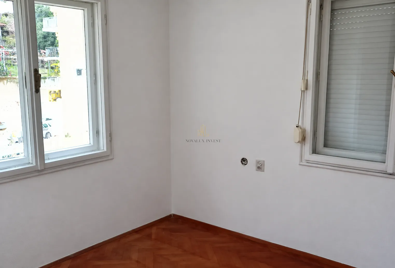 Empty room with white walls, parquet flooring and two windows.