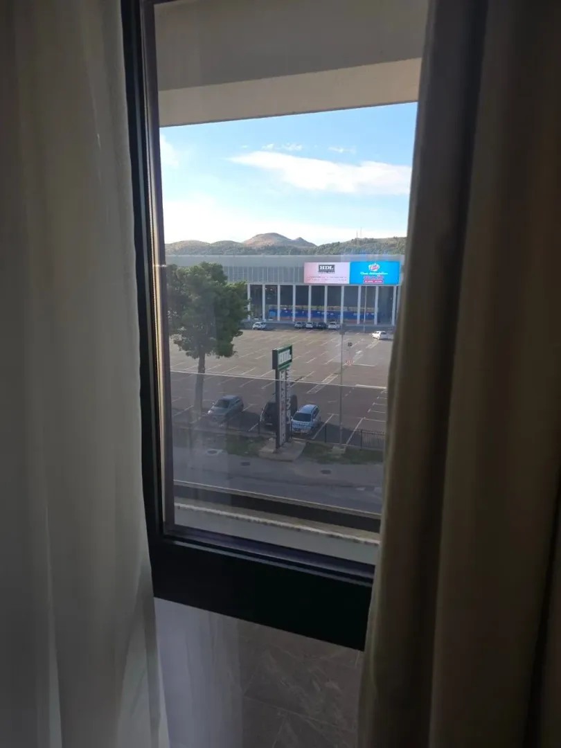 Pogled kroz prozor na parking i okolne objekte.