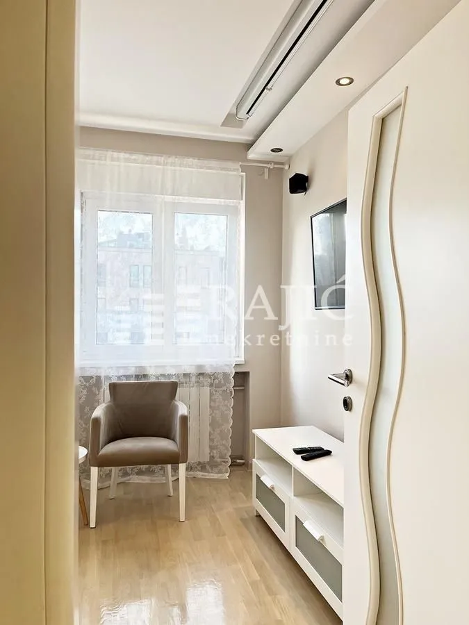 Small lit living room with an armchair, TV cabinet and a window.