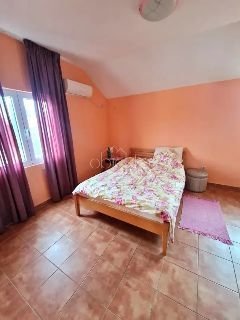 Spavaća soba sa bračnim krevetom, narandžastim zidovima i prozorom sa ljubičastim zavjesama.
