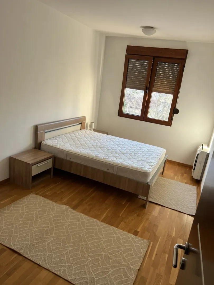 Svijetla spavaća soba sa drvenim krevetom i noćnim ormarićima.