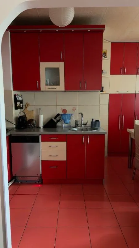 Kuhinja sa crvenim elementima i keramičkim pločicama na podu.