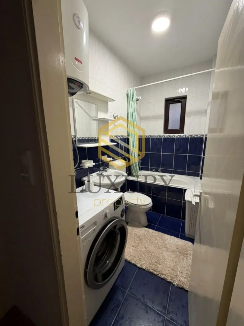 Small bathroom with a bathtub, washbasin, washing machine, and blue tiles.