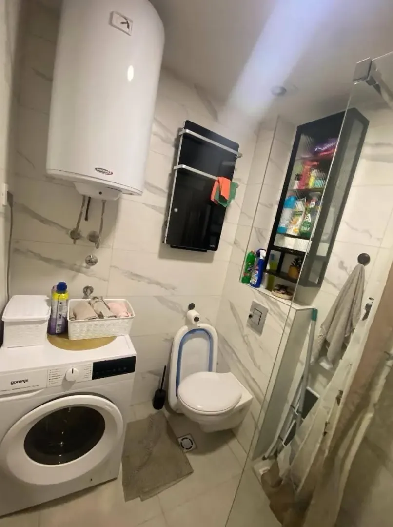 Manje kupatilo sa tuš kabinom, veš mašinom i ugrađenim sanitarijama.