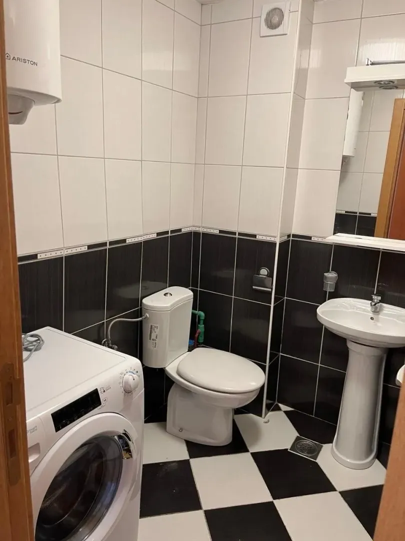 Small bathroom with white and black tiles, toilet, sink, and washing machine.