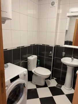 Small bathroom with white and black tiles, toilet, sink, and washing machine. - image 7