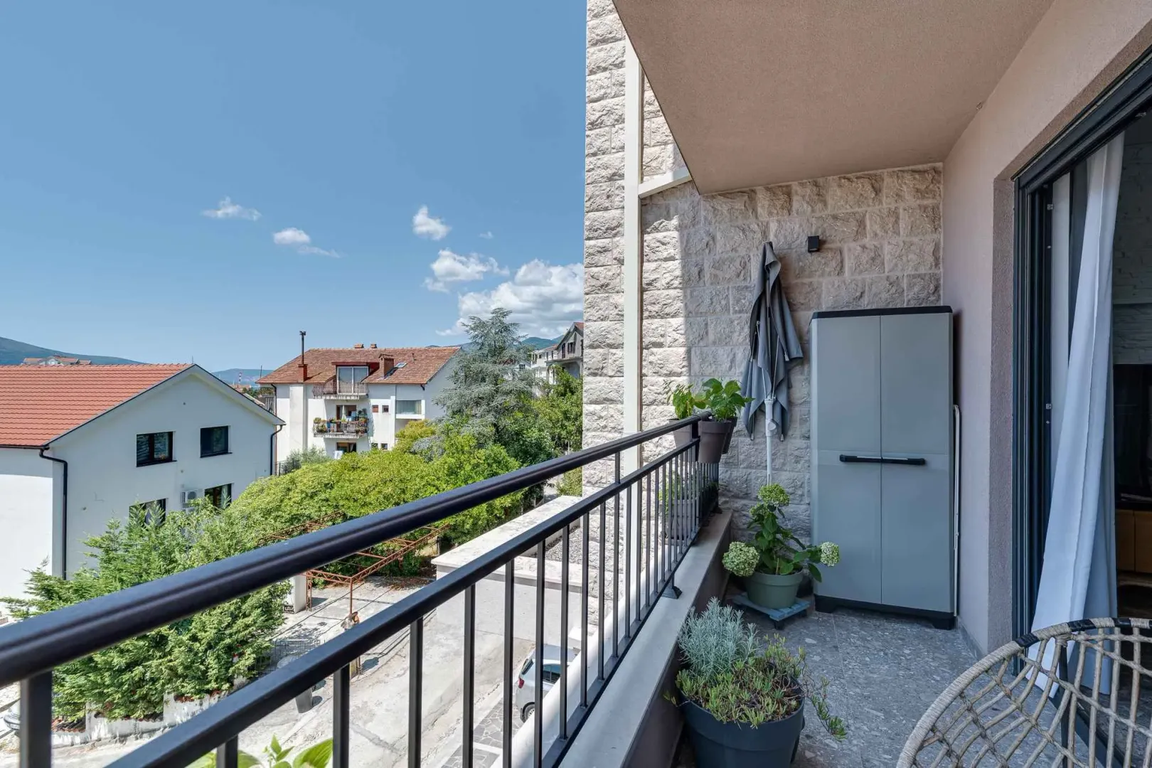 Natkriveni balkon sa pogledom na okolne zgrade i zelenilo.