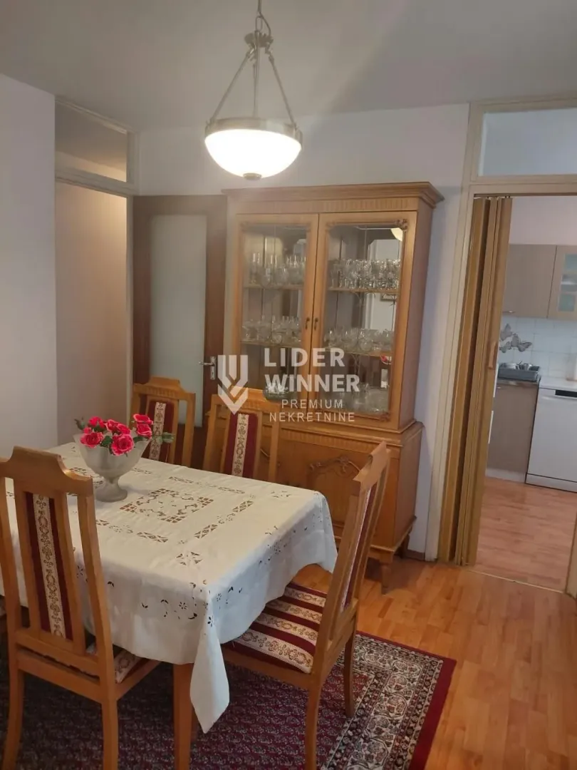 Trpezarija sa drvenim stolom, stolicama i vitrinom.