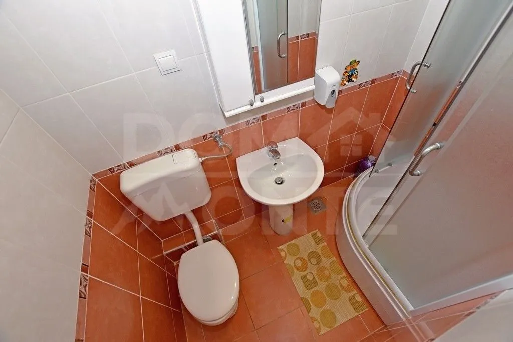 Manje kupatilo sa tuš-kabinom, umivaonikom i wc šoljom u narandžastim tonovima.
