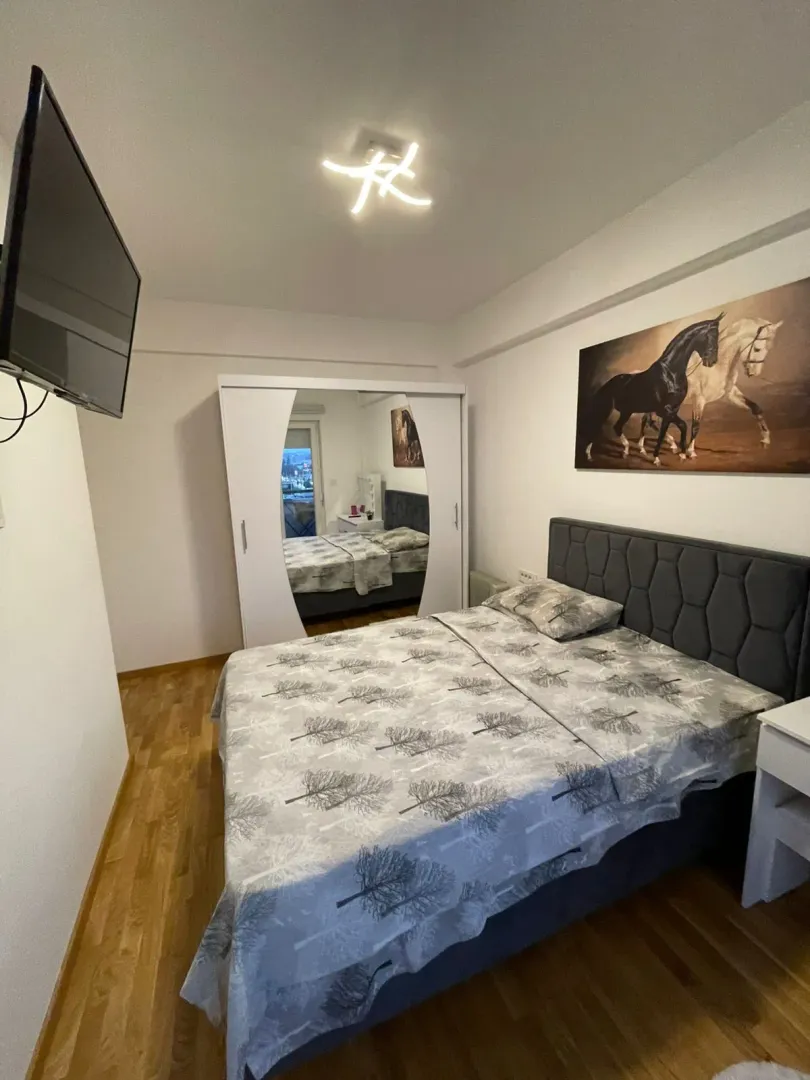 Namještena spavaća soba sa bračnim krevetom, plakarom i televizorom na zidu.