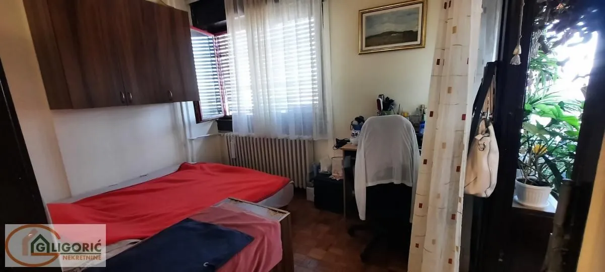 Nameštena spavaća soba sa krevetom, radnim stolom i izlazom na terasu.