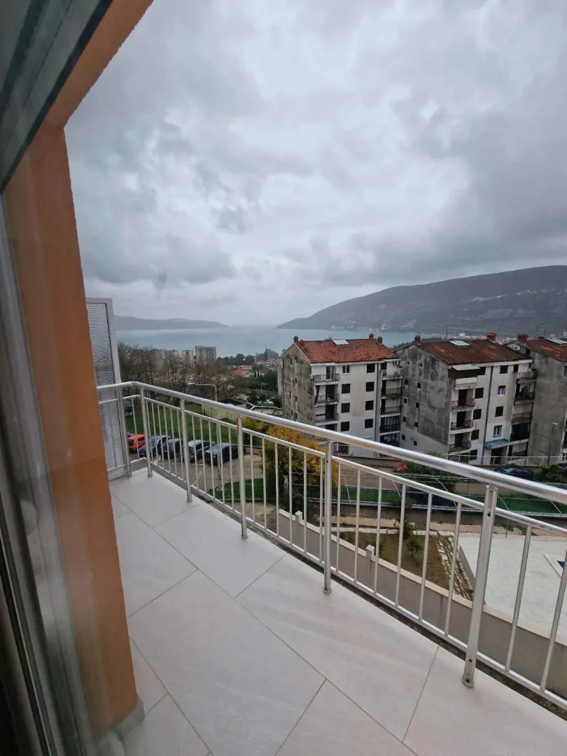 Balkon sa metalnom ogradom i pogledom na more i okolne zgrade.