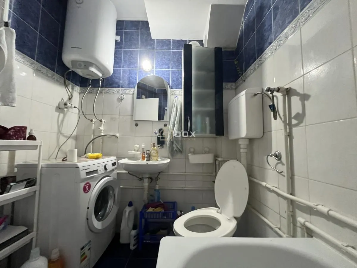 Kupatilo opremljeno sanitarijama, mašinom za veš i plavim zidnim pločicama.