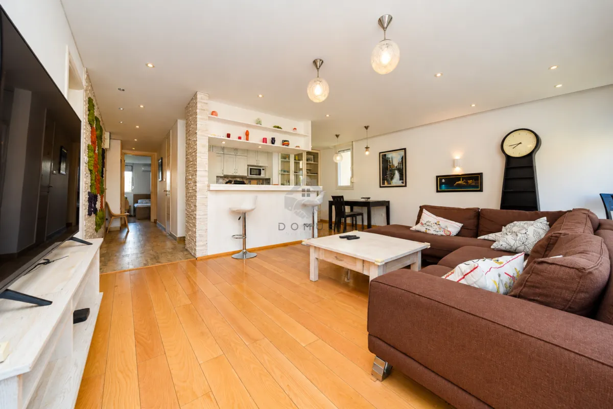 Spacious living room with a sofa, TV, and a view of the kitchen and bar.
