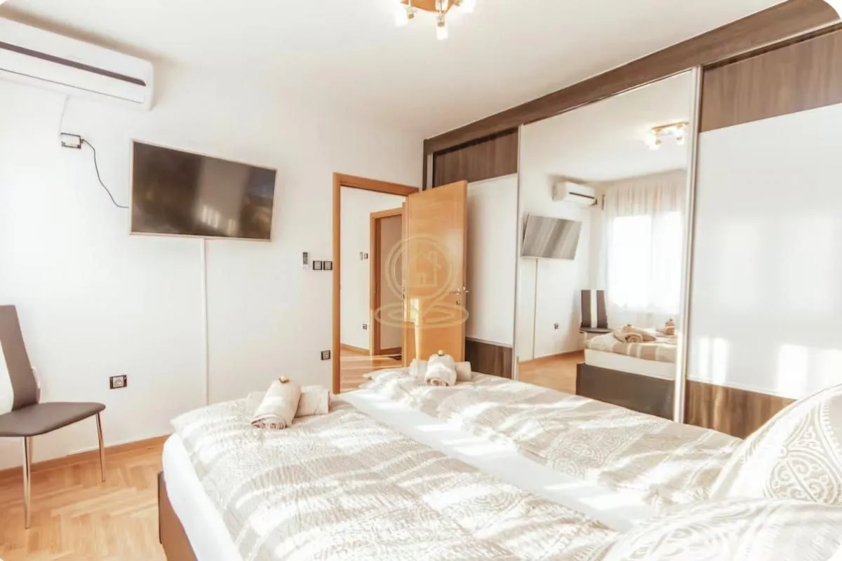 Furnished bedroom with a double bed, TV, and large mirrored wardrobe.