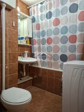 Kupatilo obloženo smeđim pločicama sa kadom i tuš zavesom. - image 9