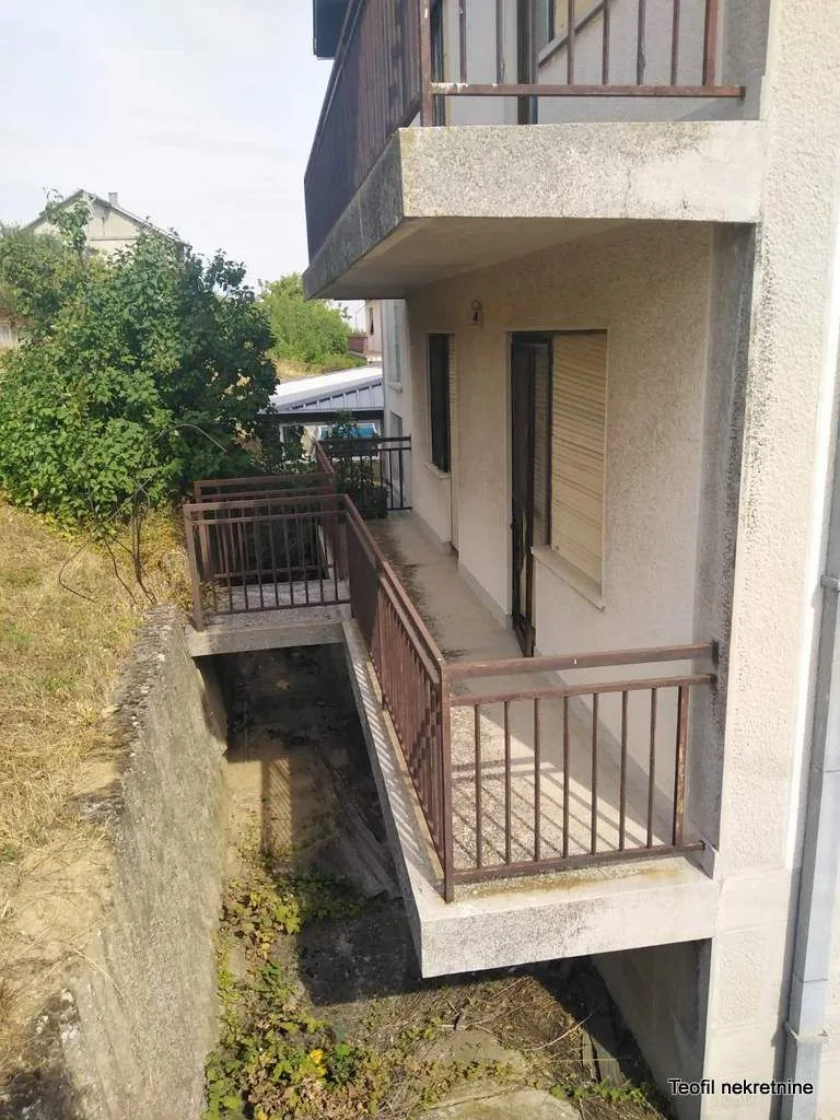 Dugački balkon sa metalnom ogradom i pogledom na okolinu.