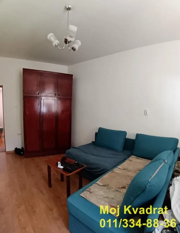 Dnevna soba sa plavom ugaonom garniturom, drvenim stočićem i ormarom.