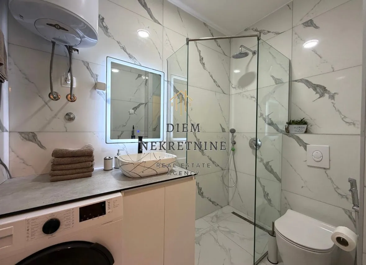 Modern bathroom with a walk-in shower, washbasin, and washing machine.