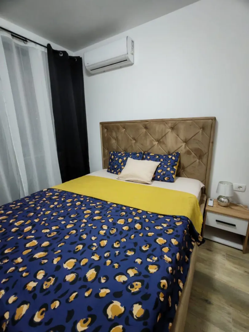 Spavaća soba sa bračnim krevetom, noćnim stočićem i klima uređajem.
