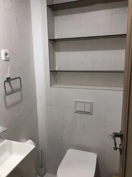 A small toilet with built-in shelves and white tiles. - image 27