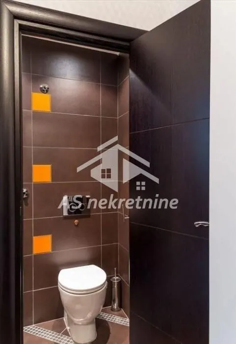 View of a modernly equipped bathroom with dark tiles and a toilet.