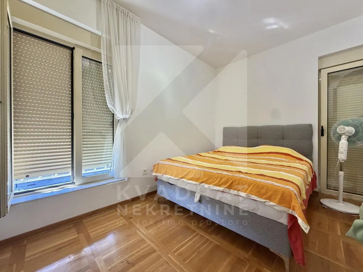 Spavaća soba sa bračnim krevetom, drvenim podom i izlazom na balkon.