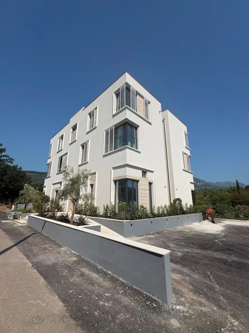 Spoljašnji izgled moderne stambene zgrade sa uređenim dvorištem.