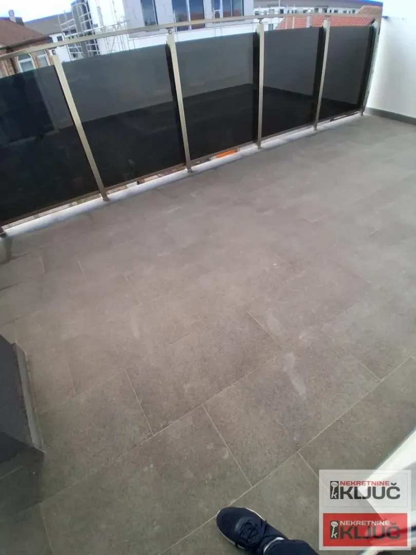 Prostrani popločani balkon sa staklenom ogradom.