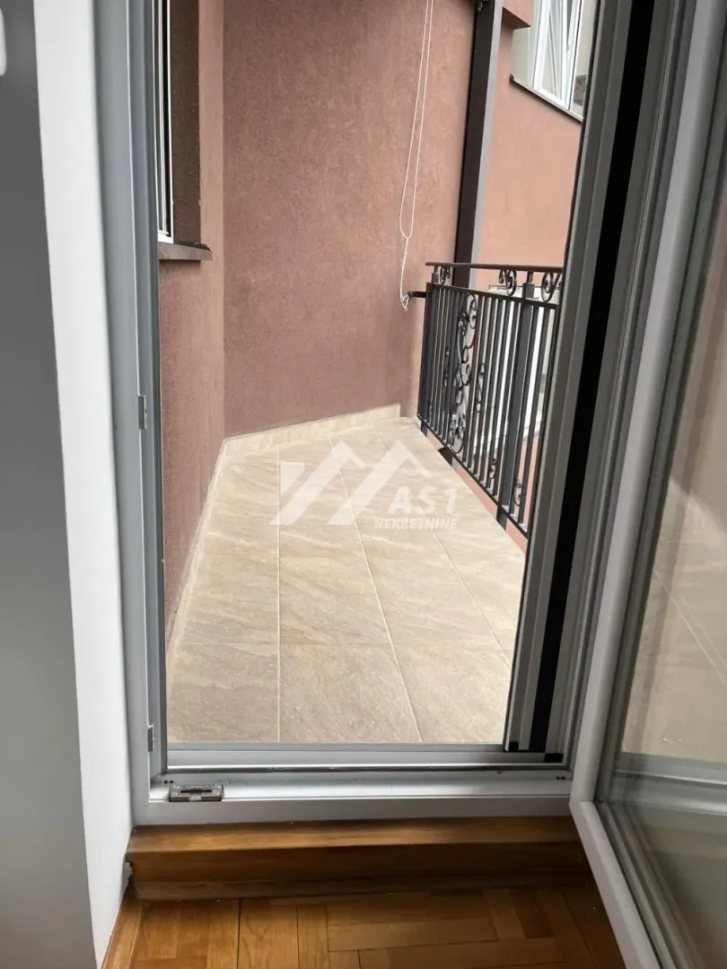 Pogled na popločanu terasu sa metalnom ogradom sa balkonskih vrata.