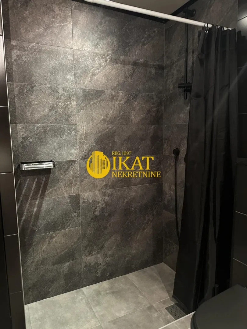 Walk-in shower with dark tiles and a black curtain in the bathroom.